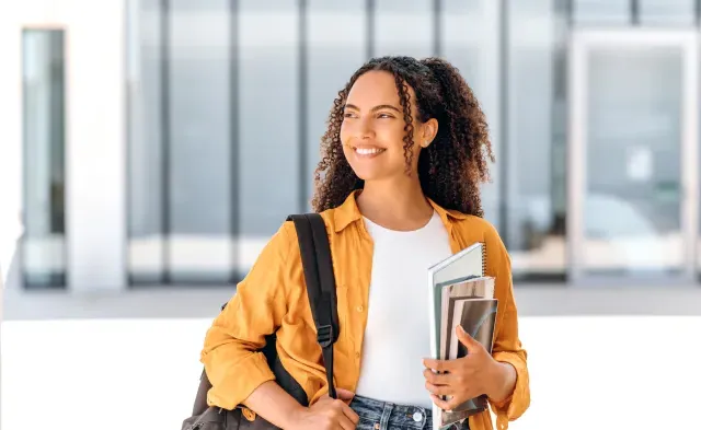 Student wearing backpack and smiling holding textbook